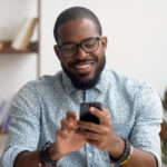 Happy african american businessman using phone mobile apps at workplace Happy african american businessman using phone mobile corporate apps at workplace texting sms, smiling black man looking at smartphone browsing internet, office technology and digital communication